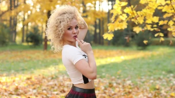 Belle femme blonde touchant les cheveux bouclés, marchant dans le parc d'automne . — Video