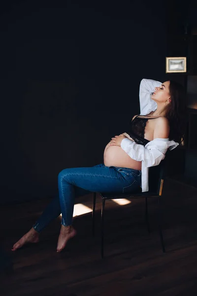 Вид сбоку беременной женщины, сидящей в кресле и позирующей — стоковое фото