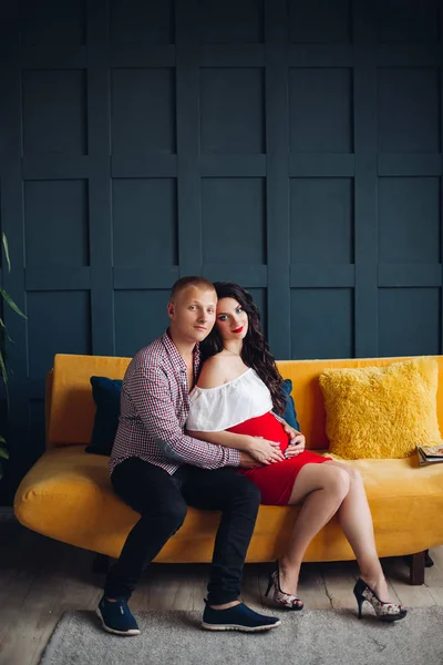 Casal elegante sentado no sofá amarelo e olhando para a câmera . — Fotografia de Stock