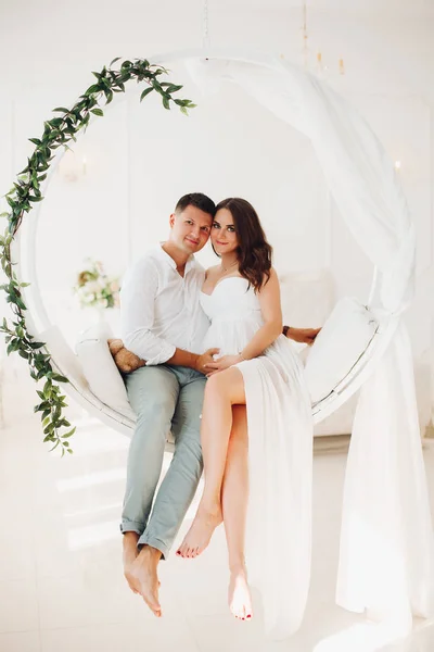 Belo casal de jovens sentados no balanço branco . — Fotografia de Stock