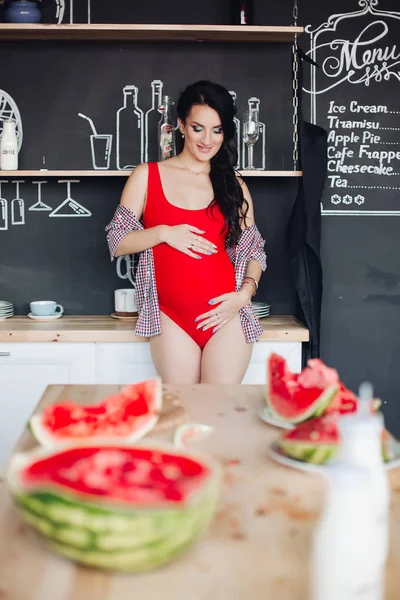 Gehalveerde heldere watermeloen op houten tafel tegen ongericht zwangere vrouw. — Stockfoto