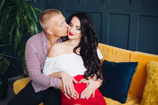 Elegante pareja sentada en un sofá amarillo y mirando a la cámara . —  Fotos de Stock