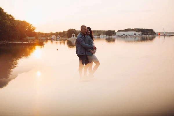 Familia esperando a un bebé parado junto al río al atardecer . —  Fotos de Stock