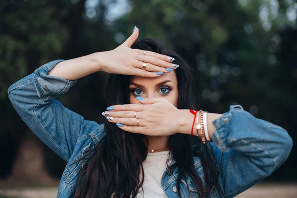 Pretty lady hiding behind hands with blue and white nails.