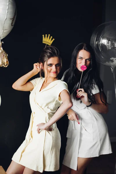 Two young ladies holding accessories and posing at camera.