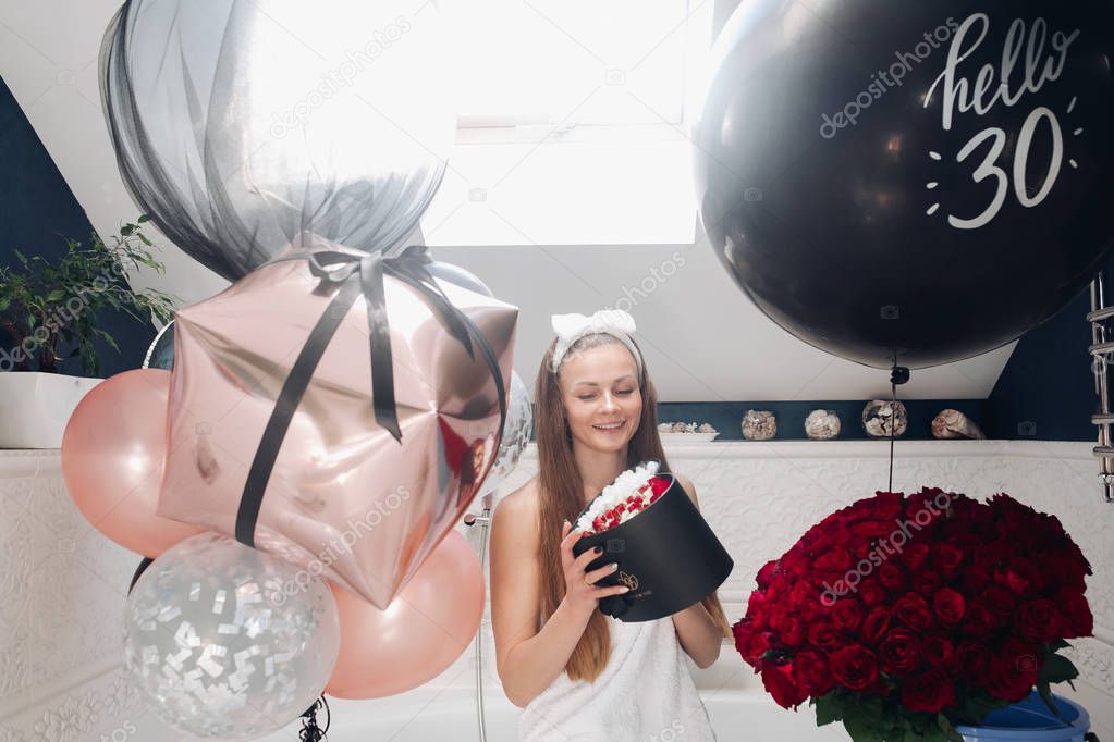 Happy adult woman with flowers and air balloons in bathroom.