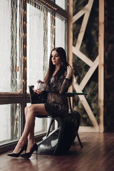 Preciosa modelo morena en vestido negro y tacones en sillón . — Foto de Stock