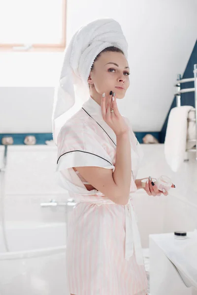 Красива молода жінка наносить крем на обличчя у ванній . — стокове фото