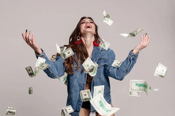 Happy laughing girl in denim jacket with flying banknotes around. — Stock Photo, Image