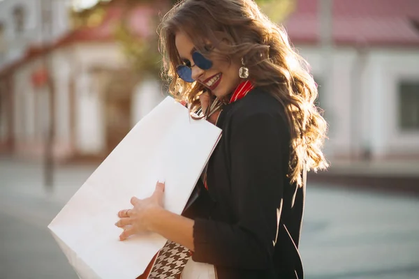 Chica morena de moda con bolsas de papel de colores, caminando por la calle . — Foto de Stock