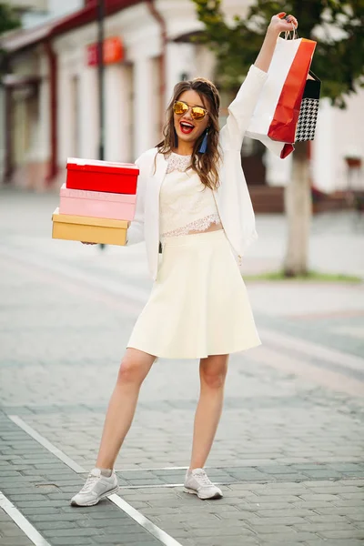 Glückliches Model im weißen Look und Sonnenbrille mit Einkaufstaschen u — Stockfoto