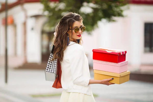 Glückliches Model im weißen Look und Sonnenbrille mit Einkaufstaschen u — Stockfoto