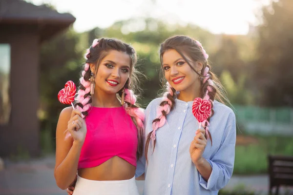 Chicas de moda con trenzas de colores con caramelos corazón en palo . — Foto de Stock