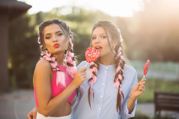 Chicas de moda con trenzas de colores con caramelos corazón en palo . — Foto de Stock