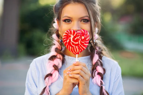 Schöne brünette Mädchen versteckt Gesicht von Süßigkeiten Herz auf Stock. — Stockfoto