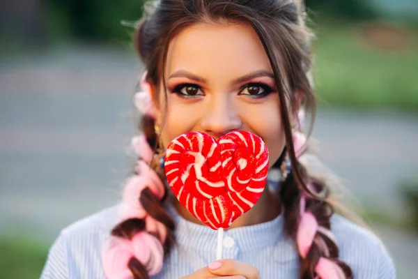 Piękna brunetka dziewczyna ukrywa twarz przez serca cukierki na kij. — Zdjęcie stockowe