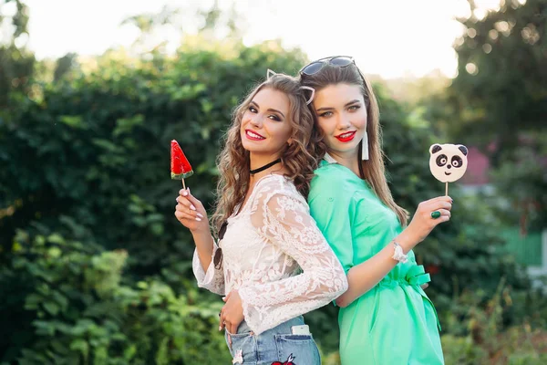 Две красивые и модные девушки держат конфеты на палочке . — стоковое фото