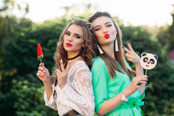 Dos novias bonitas y de moda sosteniendo caramelos en el palo . — Foto de Stock