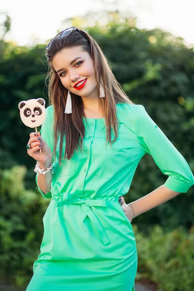 Portret van het meisje in de groene jurk met suikergoed op stok in de hand te glimlachen. — Stockfoto