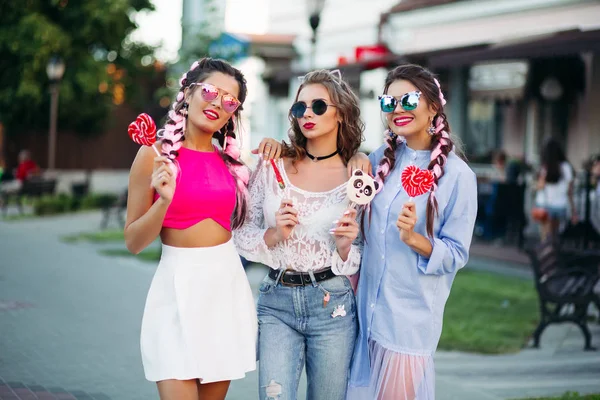 Drie mooie en trendy meisjes houden van snoepjes hart op stok. — Stockfoto