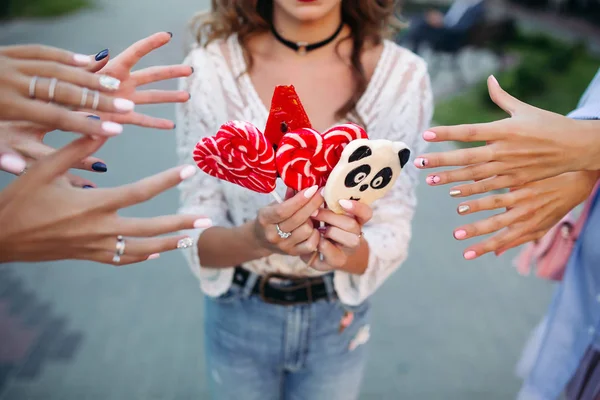 Gewas van meisje houdt van snoepjes op stok en handen van drie meisjes handen uitrekken om snoep. — Stockfoto