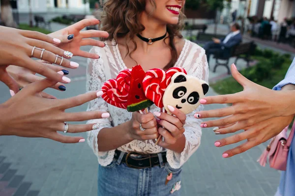 Cultivo de niña sosteniendo caramelos en palo y las manos de tres niñas estirando las manos para tomar dulces . — Foto de Stock