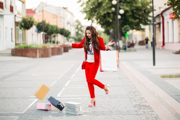 Modieuze vrouw in rode pak met boodschappentassen gedaald schoenendozen in de straat. — Stockfoto