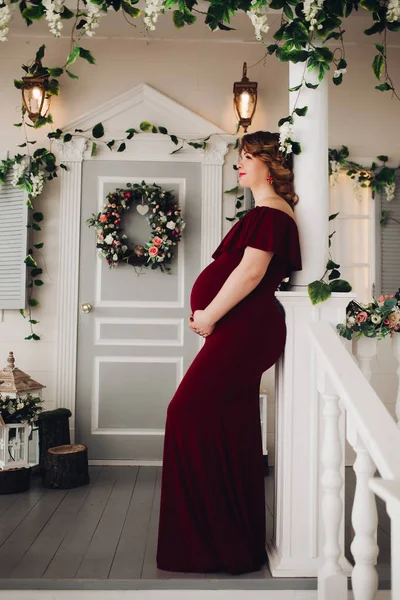 Encantadora mujer embarazada en vestido de marsala posando en los escalones de la casa . — Foto de Stock