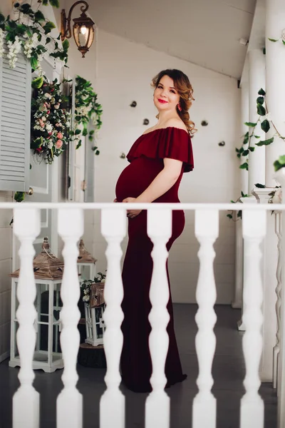 Charmante zwangere vrouw in marsala jurk poseren op trappen van huis. — Stockfoto