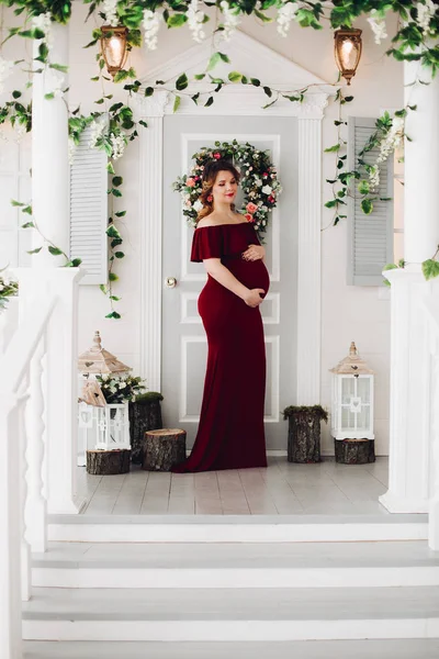 Charming pregnant woman in marsala dress posing on steps of house. — Stock Photo, Image