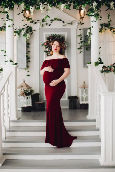 Чарівна вагітна жінка в сукні марсала позує на сходах будинку . — стокове фото
