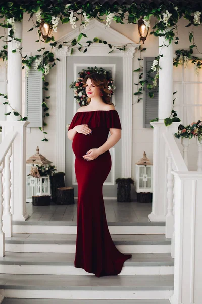 Encantadora mujer embarazada en vestido de marsala posando en los escalones de la casa . — Foto de Stock