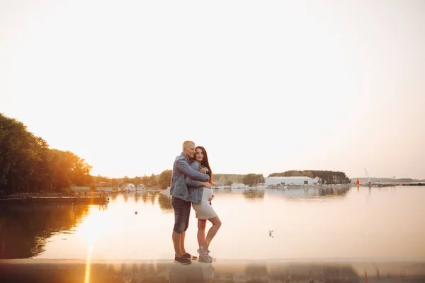 Familia esperando a un bebé parado junto al río al atardecer . —  Fotos de Stock