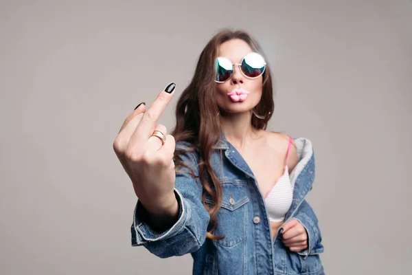 Aggressive girl in stylish sunglasses with pink plump lips showing fuck at camera. — Stock Photo, Image