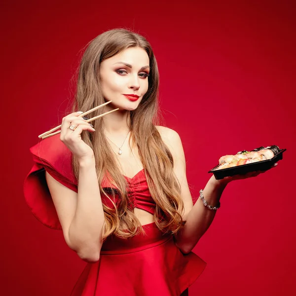 Γυναίκα με σέξι κόκκινο φόρεμα τρώει νόστιμο σούσι στο studio — Φωτογραφία Αρχείου