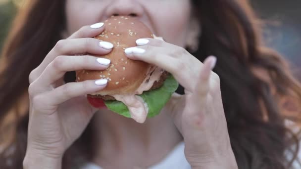Menina na moda em óculos comer hambúrguer saboroso — Vídeo de Stock
