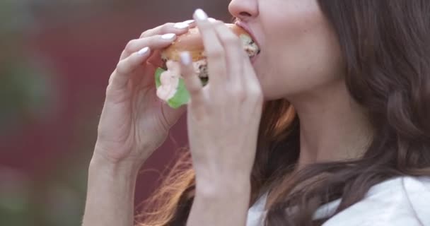Teen dívka v stylové sluneční brýle s světlé rty těší vynikající burger. — Stock video