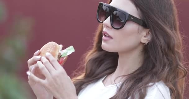 Trendiga unga flicka i glasögon äta välsmakande hamburgare — Stockvideo