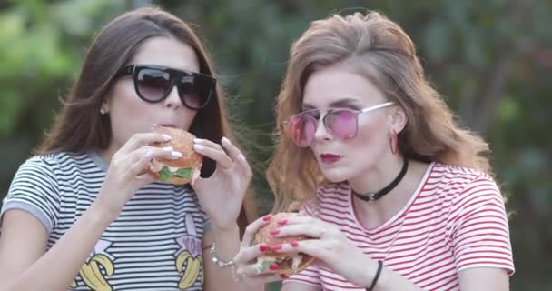 Zwei wunderschöne stilvolle Mädchen essen Hamburger. — Stockvideo