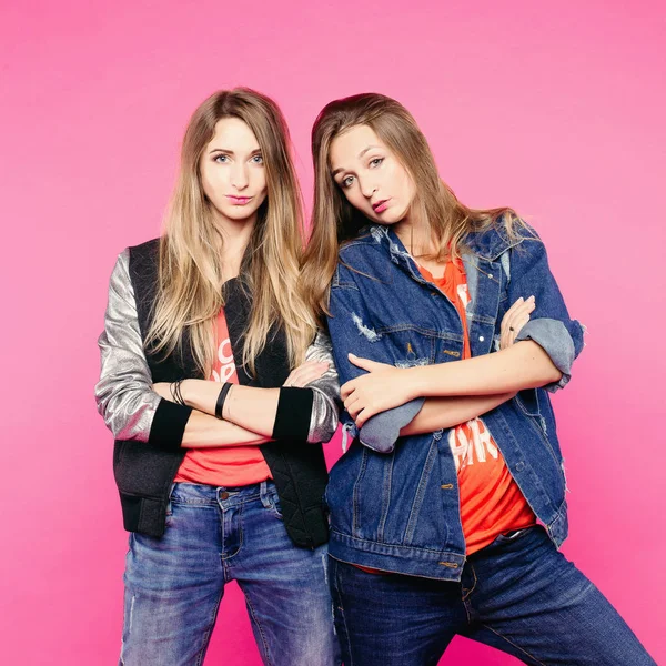 Het beeld van de lente van twee positieve meisjes met bril, vriendinnen met steil haar die knuffel, kijk naar de camera. Een meisje een denim jasje zet een vriendinnen hoorns. In kleding van alledaagse stijl en glazen. — Stockfoto