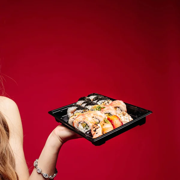 Beautiful brunette young woman with box of sushi and sticks on red.