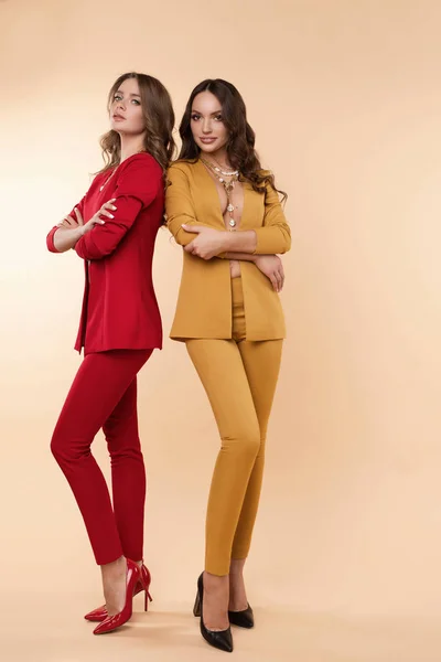 Dos modelos magníficos en trajes de colores y tacones altos sobre fondo plano . — Foto de Stock