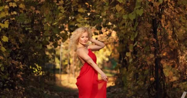 Beautiful and sexy blonde woman in long red dress walking in autumn park. — Stock Video