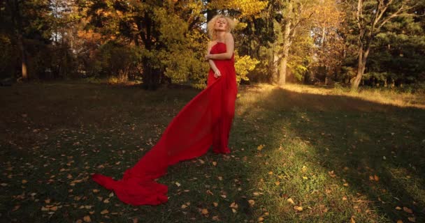 Mooi en sexy blonde vrouw in lange rode jurk wandelen in de herfst park. — Stockvideo