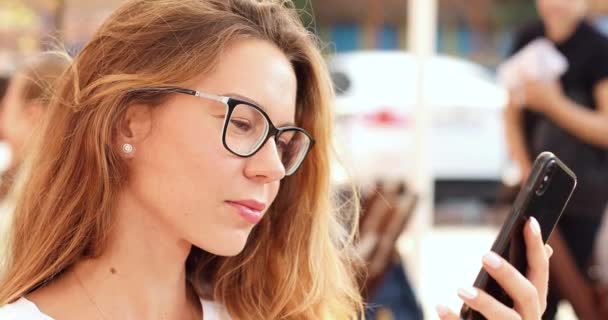 Красивая молодая девушка в очках в Интернете в кафе на открытом воздухе . — стоковое видео