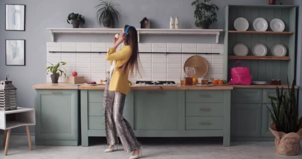 Lycklig ung flicka i moderiktiga kläder dansa i köket. — Stockvideo