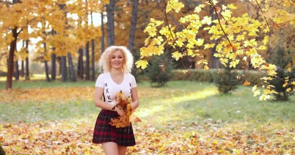 Mujer rubia feliz en top de la cosecha sexy y falda jugando con el follaje en el parque . — Vídeos de Stock