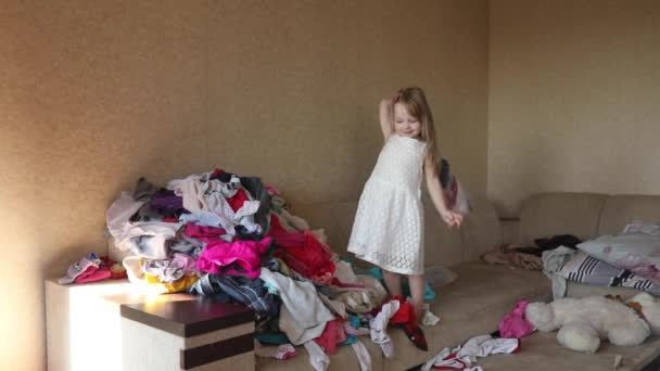Petite fille en robe jetant des vêtements sur le canapé . — Video