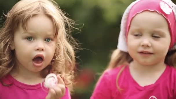 Чарівні маленькі дівчата в літніх капелюхах їдять смачне печиво в саду . — стокове відео