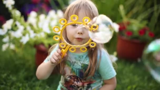 Super cute fair-haired little girl in t-shirt blowing soap bubbles on grass. — Stock Video